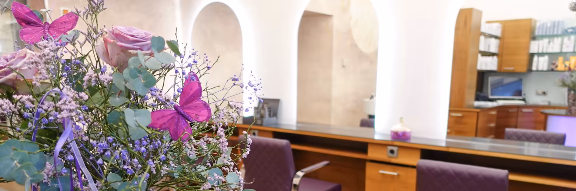Empfaqng Friseursalon Birgit Gmeiner Ein Blumenstrauß mit lila Schmetterlingen im Empfangsbereich vom Friseursalon Birgit Gmeiner mit Blick auf den hellen, modernen Salonbereich.
