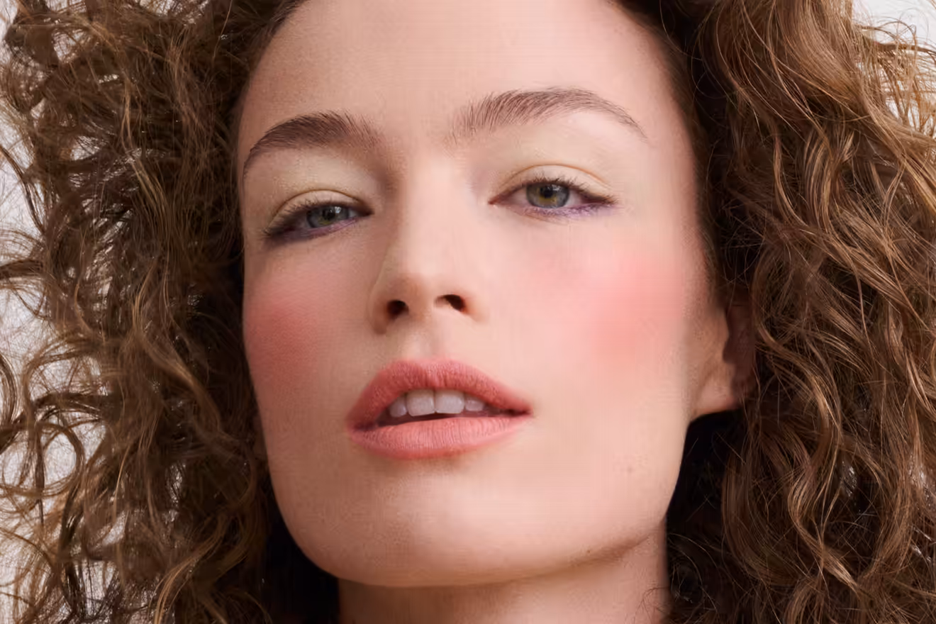 Nahaufnahme einer Frau mit lockigem Haar und präzisem Look Ink Line Augen-Make-up, das ihre Augen betont und einen natürlichen Teint unterstreicht.